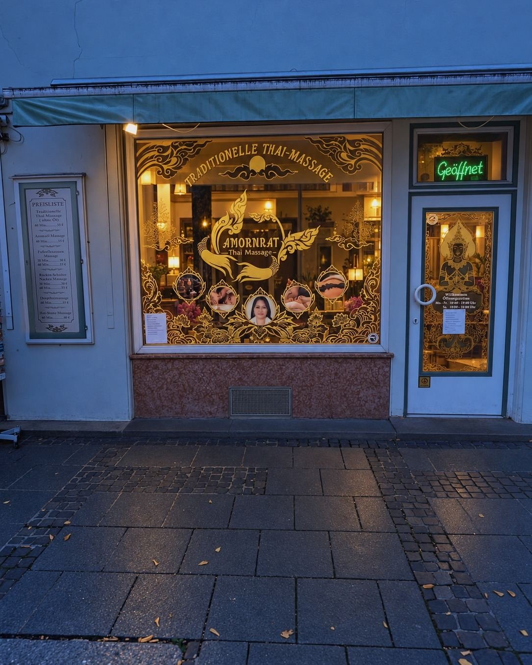 Eingang von Amornrat Thai Massage in der Ludwigstraße 6 in der Dämmerung, das Schaufenster mit goldener Schrift leuchtet warm