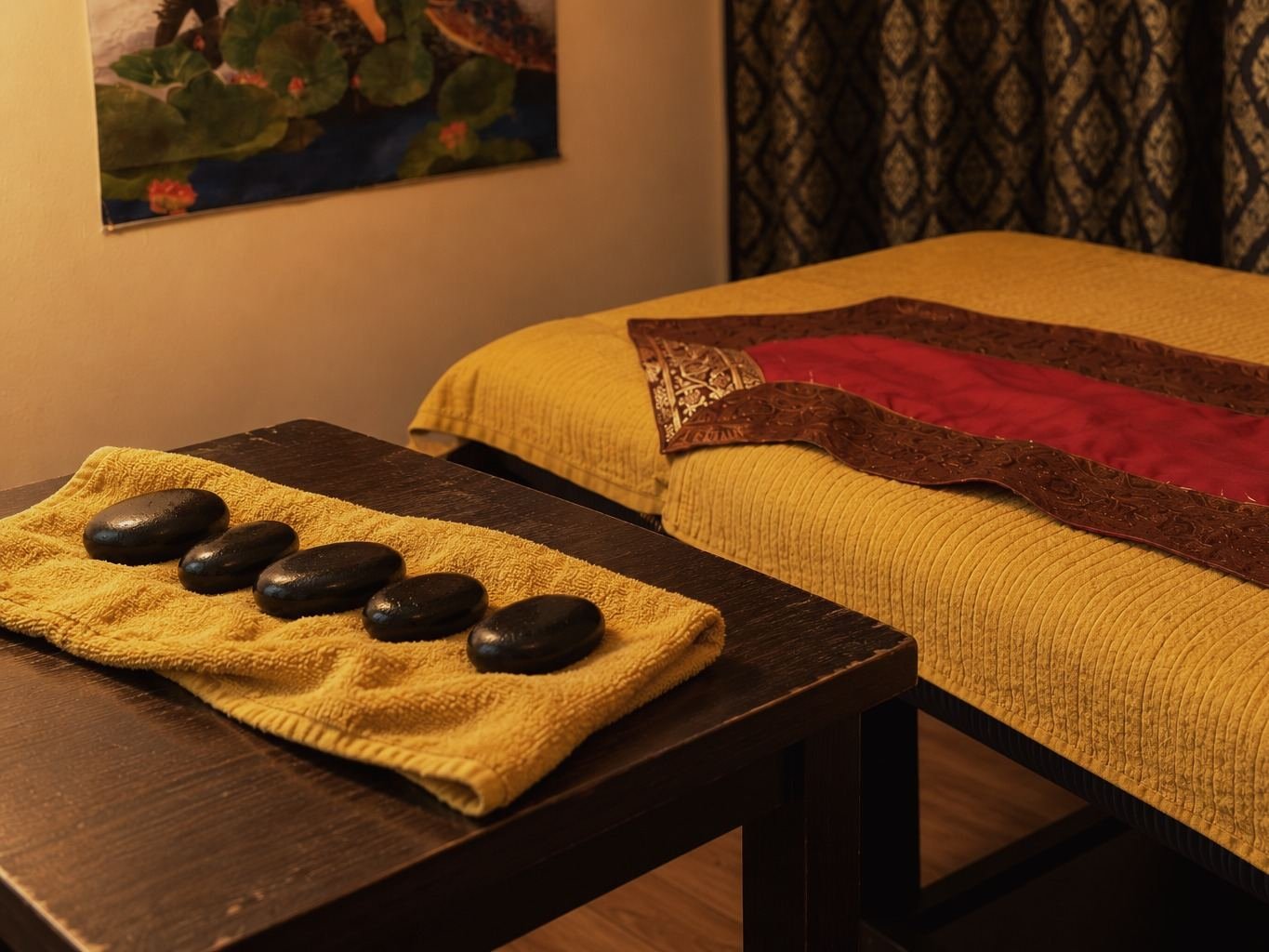 Fünf glatte schwarze Steine auf einem senfgelben Handtuch neben einer Massageliege